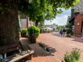 Ein lauschiger Kirchplatz in Recklinghausen mit Kopfsteinpflaster, Bäumen und Sitzgelegenheiten. Ein Paar spaziert vorbei an Cafés mit Außenbestuhlung.