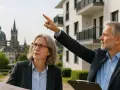 Immobilienpreise Aachen: Ein Mann zeigt auf ein neues Gebäude, während eine Frau Pläne studiert. Im Hintergrund die Aachener Domkuppeln.