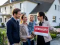 Glückliche Familie vor Haus mit "Verkauft"-Schild. Die Immobilienpreise in Siegen sind im Aufwind, und dieses Haus hat schnell einen neuen Besitzer gefunden.