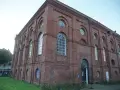 Das imposante Backsteingebäude der Zeche Scherlbeck mit seinen vielen Rund- und Bogenfenstern, einige davon bunt beleuchtet, strahlt historischen Charme aus.