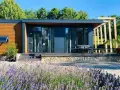 Modernes tiny house im garten der eltern, umgeben von Lavendel und Bäumen. Eine Terrasse mit Sitzmöbeln lädt zum Entspannen ein.