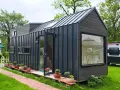 Modernes Tiny House als Anbau mit dunkler Fassade, Glasfront und vielen Pflanzen.