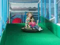 Zwei lachende Mädchen rutschen auf einem Schlauchboot in einem Indoor-Spielplatz.