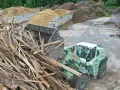 Radlader sammelt Holzreste für die Wiederverwertung. Große Haufen von recycelten Materialien sind im Hintergrund zu sehen.
