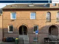Ziegelhaus mit mehreren Fenstern und Eingängen. Ein Parkplatzschild weist auf die Lage hin, die für die Neuss Immobilienpreise relevant ist.