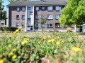 Grünes Gras mit Löwenzahn vor einem Mehrfamilienhaus in Wesel. Hier könnte man sich über den Mietspiegel Wesel informieren.