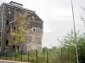 Ein verlassener Malakowturm aus dunklem Backstein, umgeben von Bäumen im Herbstlaub.