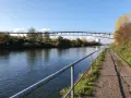 Ein Radweg am Rhein-Herne-Kanal führt unter einer modernen Brücke hindurch. Herbstlaub schmückt die Ufer.