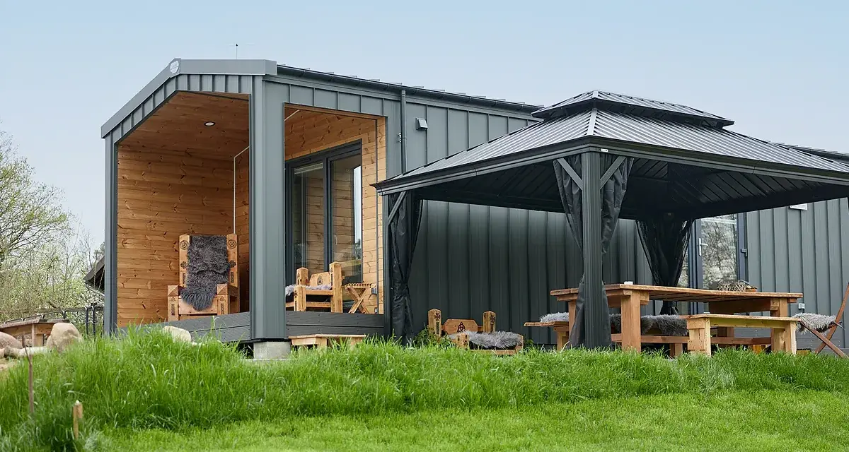 Modernes Tiny House mit Holzveranda, Sitzmöbeln und Pavillon. Ein Beispiel für die Tiny house movement, das minimalistisches Wohnen im Grünen ermöglicht.