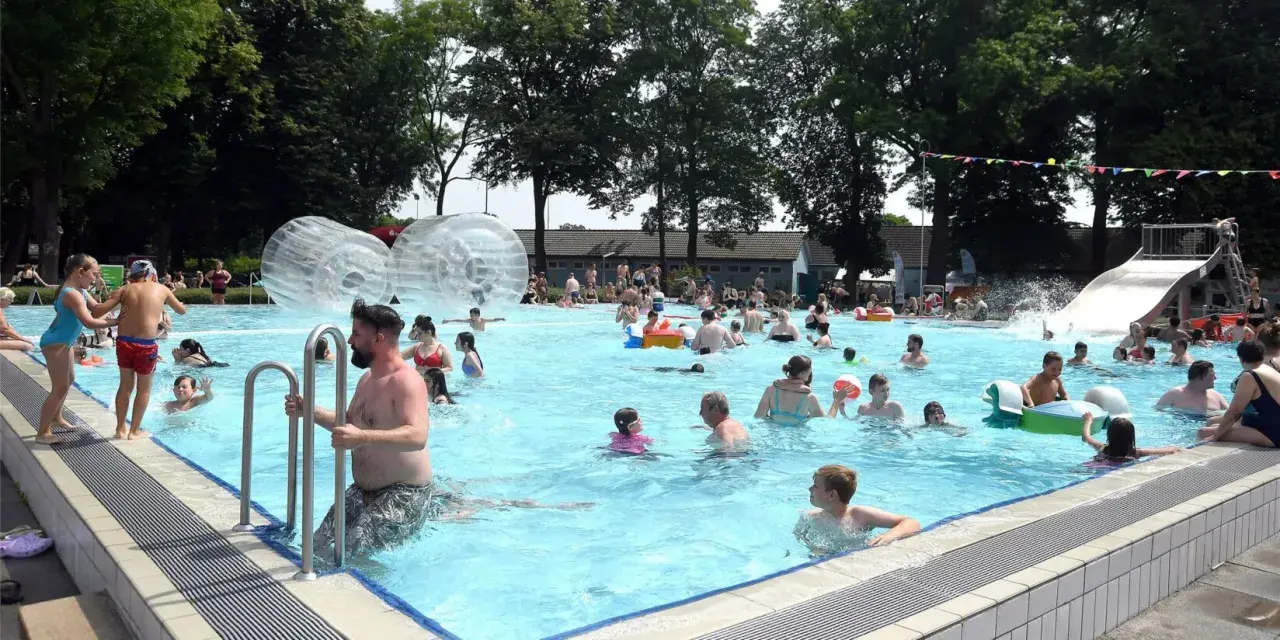 Menschen genießen einen sonnigen Tag im Parkbad Nord. Kinder planschen, rutschen und spielen in den Wasserbällen.