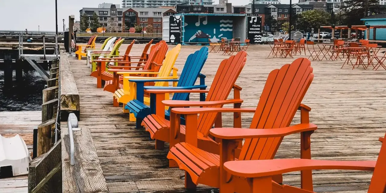 Reihe bunter Adirondack-Stühle am Kai. Die Haard ist leer, aber die Stühle laden zum Verweilen ein.