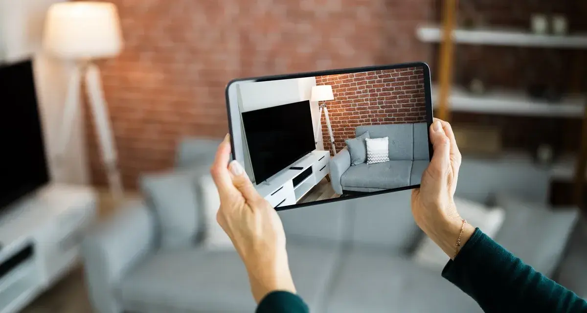Hände halten Smartphone, das eine Wohnung mit Sofa und Fernseher zeigt. Darf ein Makler Fotos von meiner Wohnung machen? Ja, für die Vermarktung.