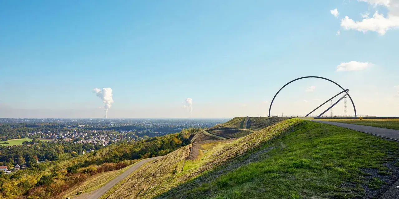Blick über die Halde Recklinghausen mit der markanten Hängebrücke und rauchenden Schloten in der Ferne.