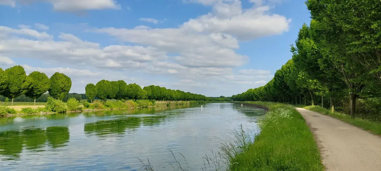 Ein ruhiger Tag am Dortmund-Ems-Kanal. Grüne Bäume säumen das Ufer, ein Weg lädt zum Spazieren ein.