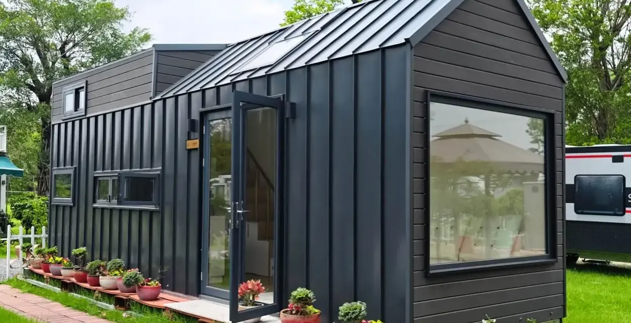 Modernes Tiny House als Anbau mit dunkler Fassade, Glasfront und vielen Pflanzen.