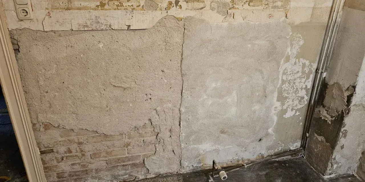 Abblätternder Putz an einer Wand mit freiliegenden Ziegeln und einer Steckdose. Vorsicht bei der Renovierung, um **asbest erkennen** zu können.