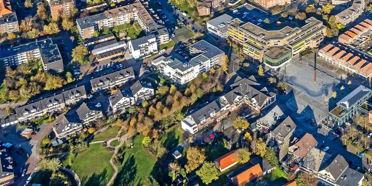 Luftaufnahme eines Wohngebiets mit Mehrfamilienhäusern und Einfamilienhäusern. Die Bäume zeigen Herbstlaub. Ein zentraler Platz ist zu sehen. Hier könnte man den Mietspiegel Voerde studieren.