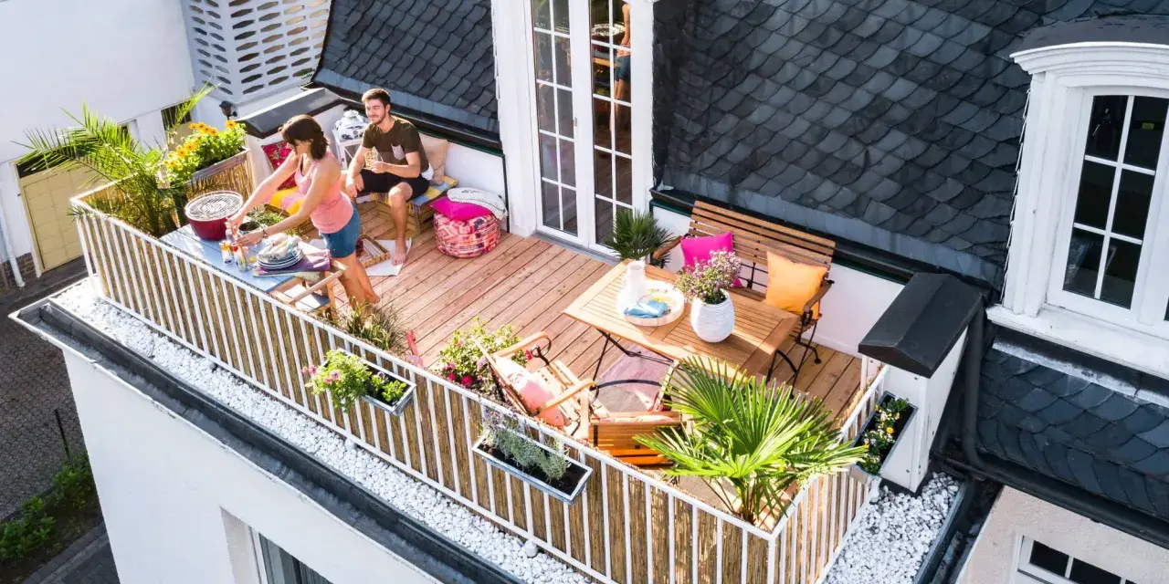 Ein Paar genießt den Sommer auf einem Balkon mit Holz-Bodenbelag, ideal für eine Mietwohnung. Grillen und Entspannen stehen im Vordergrund.
