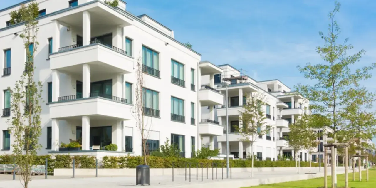 Moderne weiße Wohnanlage mit Balkonen und Bäumen. Ein Blick auf den Quadratmeterpreis Eigentumswohnung in dieser Gegend.