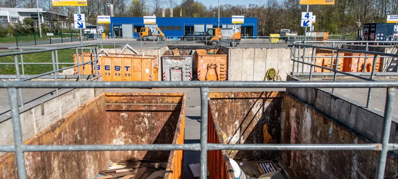 Große orange Container auf einem Recyclinghof in Bottrop. Ein kleiner gelber Bagger steht bereit.