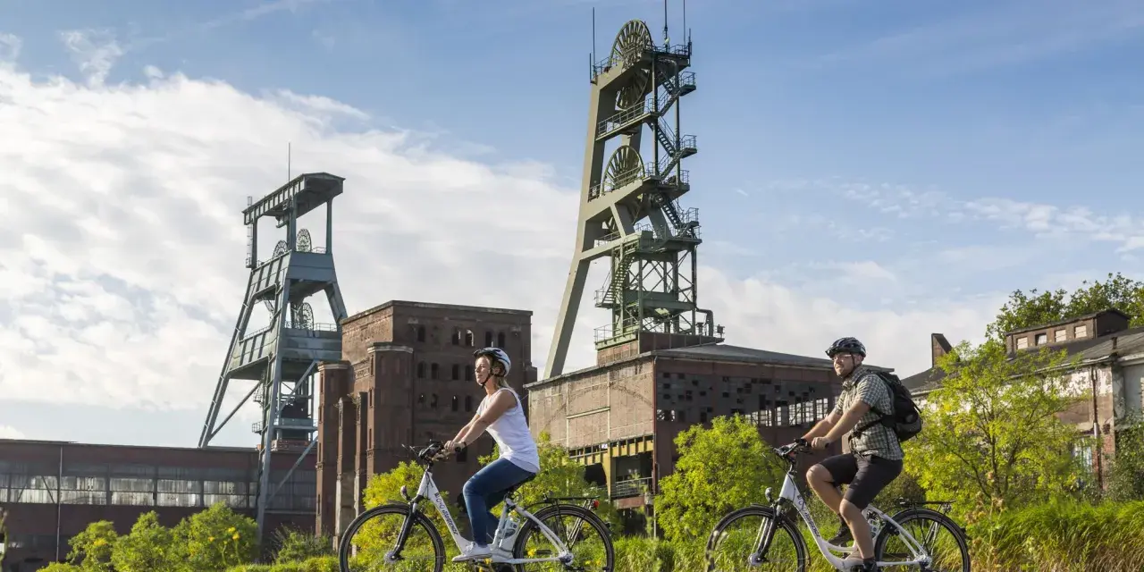Zwei Radfahrer genießen die Aussicht auf die beeindruckenden Fördertürme der Zeche Ewald, ein Symbol für Industriegeschichte und neuen Freizeitwert.