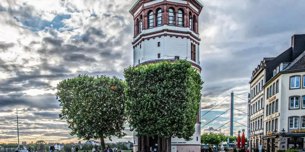 Düsseldorfer Rheinturm mit Bäumen und Gebäuden. Die Immobilienpreise in Oberbilk sind ein Thema, das viele interessiert.