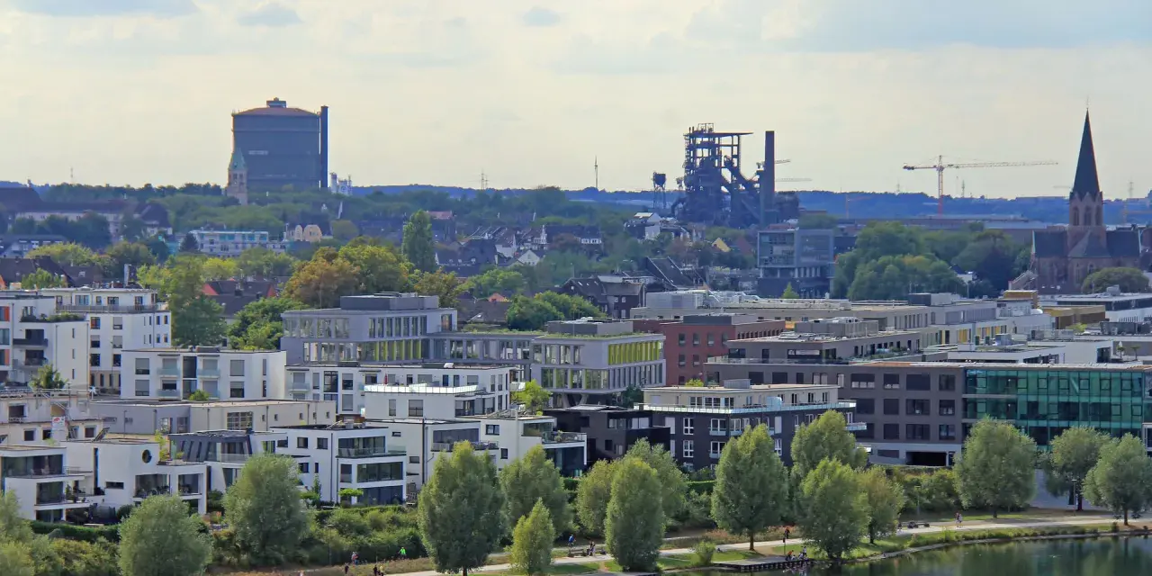 Moderne Wohngebäude am Wasser, im Hintergrund Industriedenkmäler und eine Kirche. Der Wohnungsmarkt Dortmund zeigt sich hier von seiner modernen Seite.