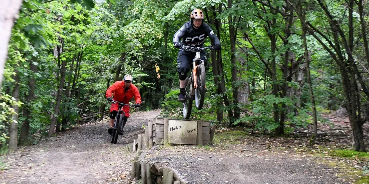 Zwei Mountainbiker springen über die Holzbox auf dem Halde Hoppenbruch Trail.