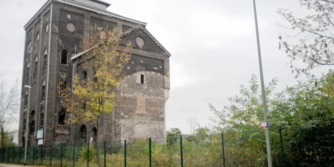 Ein verlassener Malakowturm aus dunklem Backstein, umgeben von Bäumen im Herbstlaub.