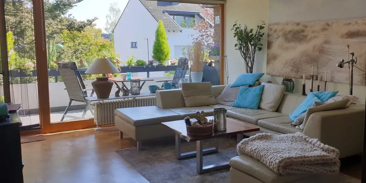 Gemütliches Wohnzimmer mit Ledercouch, Blick auf Balkon und Garten. Ein schönes Zuhause, das die Immobilienpreise in Ratingen widerspiegelt.