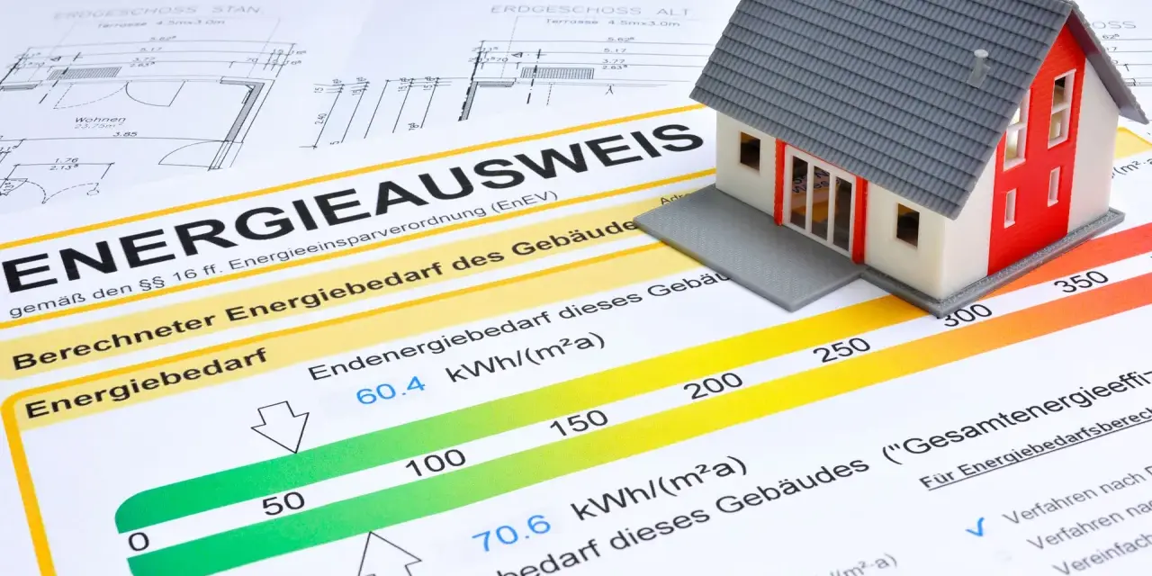 Modellhaus auf einem Energieausweis (Verbrauchsausweis oder Bedarfsausweis). Der Ausweis zeigt den Energiebedarf eines Gebäudes mit einer Skala von grün bis rot.