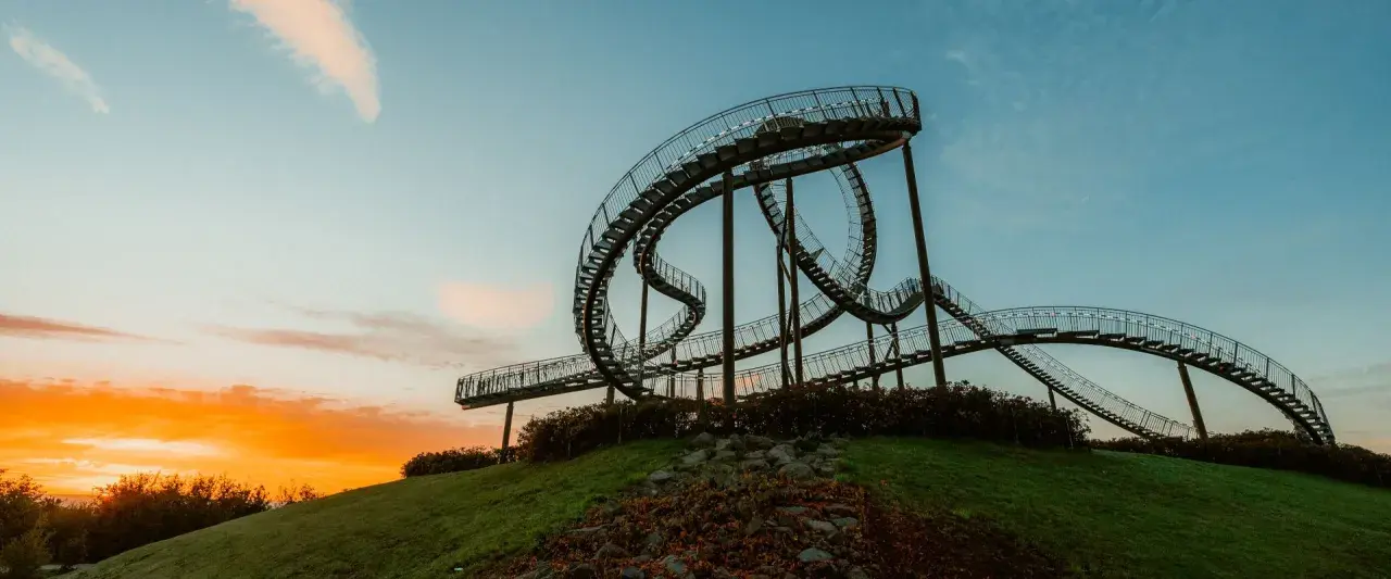 Die Achterbahn-Skulptur Tiger & Turtle auf einer Halde im Ruhrgebiet, im warmen Licht des Sonnenuntergangs.