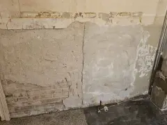 Abblätternder Putz an einer Wand mit freiliegenden Ziegeln und einer Steckdose. Vorsicht bei der Renovierung, um **asbest erkennen** zu können.