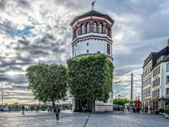 Düsseldorfer Rheinturm mit Bäumen und Gebäuden. Die Immobilienpreise in Oberbilk sind ein Thema, das viele interessiert.