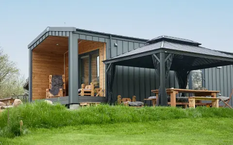 Modernes Tiny House mit Holzveranda, Sitzmöbeln und Pavillon. Ein Beispiel für die Tiny house movement, das minimalistisches Wohnen im Grünen ermöglicht.