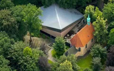 Luftaufnahme von Annaberg Haltern: Ein Gotteshaus mit rotem Ziegeldach und grüner Turmspitze, daneben ein moderner Bau mit Pyramiden-Dach, umgeben von üppigem Grün.