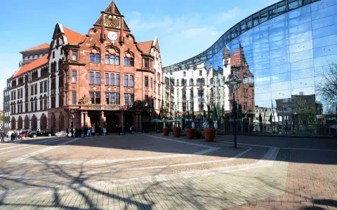 Historisches Gebäude und moderne Glasfassade spiegeln sich auf dem Platz. Hier könnte man sich über den Mietspiegel Dortmund informieren.