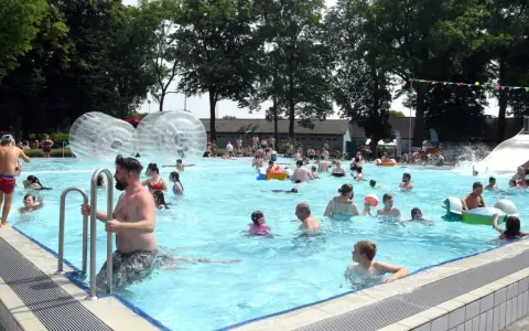 Menschen genießen einen sonnigen Tag im Parkbad Nord. Kinder planschen, rutschen und spielen in den Wasserbällen.