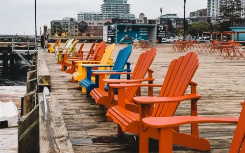 Reihe bunter Adirondack-Stühle am Kai. Die Haard ist leer, aber die Stühle laden zum Verweilen ein.