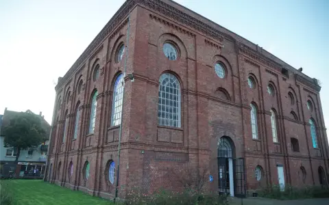 Das imposante Backsteingebäude der Zeche Scherlbeck mit seinen vielen Rund- und Bogenfenstern, einige davon bunt beleuchtet, strahlt historischen Charme aus.