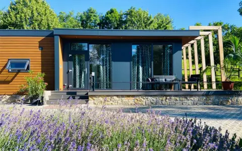 Modernes tiny house im garten der eltern, umgeben von Lavendel und Bäumen. Eine Terrasse mit Sitzmöbeln lädt zum Entspannen ein.