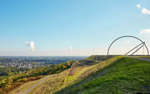 Blick über die Halde Recklinghausen mit der markanten Hängebrücke und rauchenden Schloten in der Ferne.