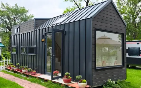 Modernes Tiny House als Anbau mit dunkler Fassade, Glasfront und vielen Pflanzen.