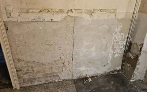 Abblätternder Putz an einer Wand mit freiliegenden Ziegeln und einer Steckdose. Vorsicht bei der Renovierung, um **asbest erkennen** zu können.
