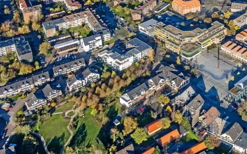 Luftaufnahme eines Wohngebiets mit Mehrfamilienhäusern und Einfamilienhäusern. Die Bäume zeigen Herbstlaub. Ein zentraler Platz ist zu sehen. Hier könnte man den Mietspiegel Voerde studieren.