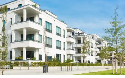Moderne weiße Wohnanlage mit Balkonen und Bäumen. Ein Blick auf den Quadratmeterpreis Eigentumswohnung in dieser Gegend.
