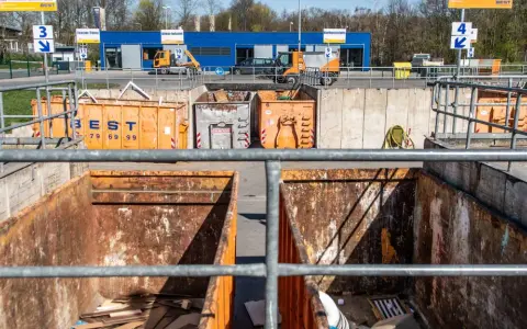 Große orange Container auf einem Recyclinghof in Bottrop. Ein kleiner gelber Bagger steht bereit.