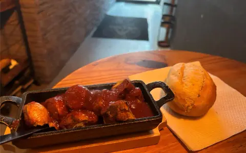 Herzhafte Steiger Wurst in Tomatensoße mit einem Brötchen auf einem Holztisch.