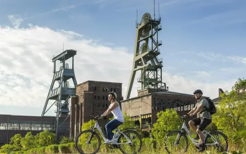 Ein Paar genießt eine Fahrradtour in Recklinghausen, vorbei an alten Fördertürmen und Industriegebäuden.