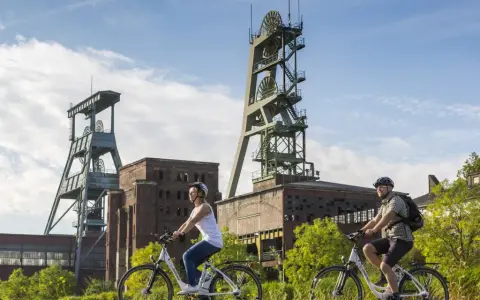 Zwei Radfahrer genießen die Aussicht auf die beeindruckenden Fördertürme der Zeche Ewald, ein Symbol für Industriegeschichte und neuen Freizeitwert.